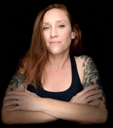 Black and white studio portrait of Katy Simmons, arms folded, looking directly at the camera