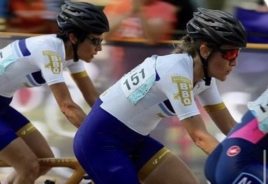 Katy Simmons riding in a tight criterium pack wearing number 151, cornering low on a closed street course